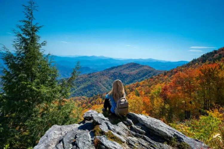 Girl sitting on the rock on top of the mountain enjoying beautiful autumn scenery