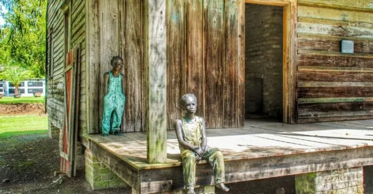 Statue of two kid one sitting on the floor next to a pillar and one standing