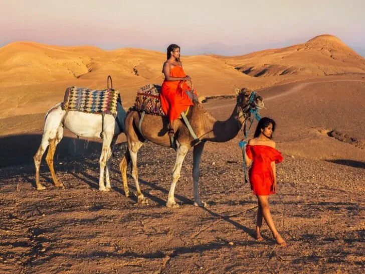 women in red with a camel in a dessert in Marrakech