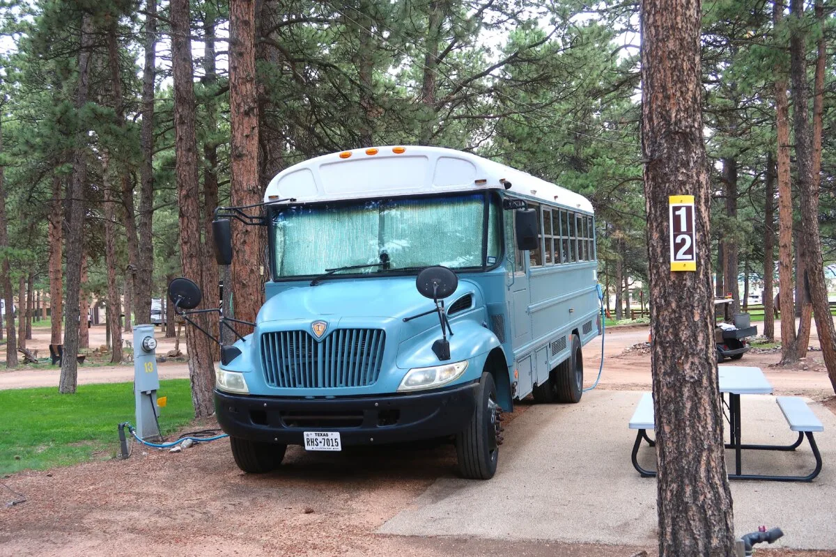 Camping vehicle in a wooded campground. Blue school bus converted into camper. Living out of a bus. House on wheels. Tiny house