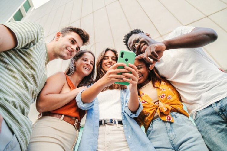Low angle view of multiracial group of young friends enjoying and smiling using their mobile phone 