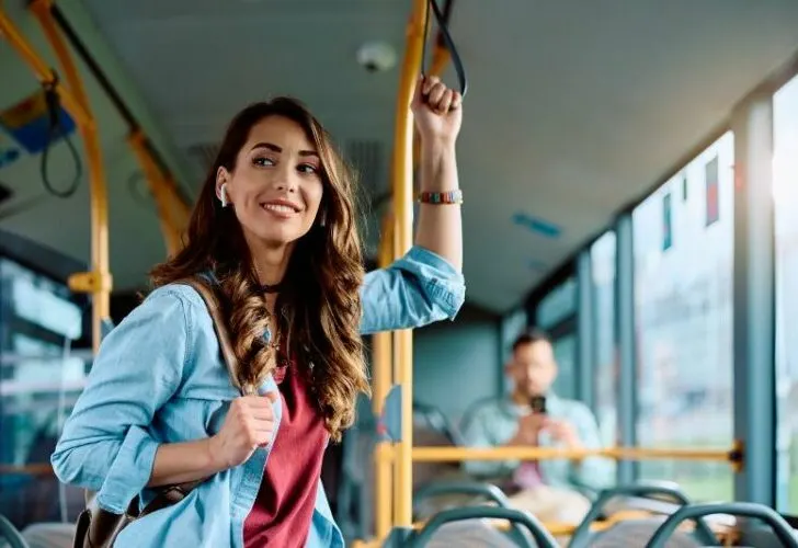 Young smiling woman holds onto handle while traveling by bus