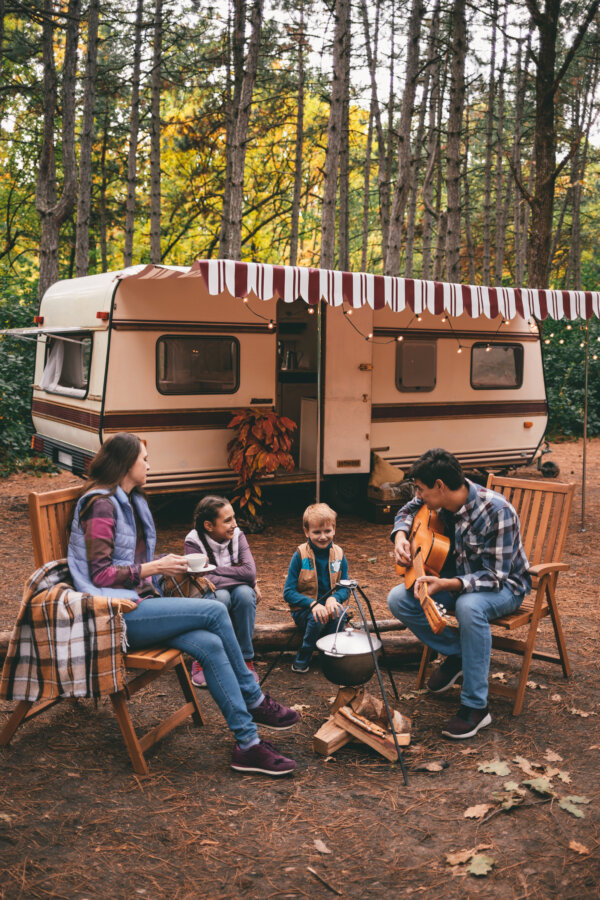 Happy family with a camping trailer on a camping trip relaxing in the autumn forest