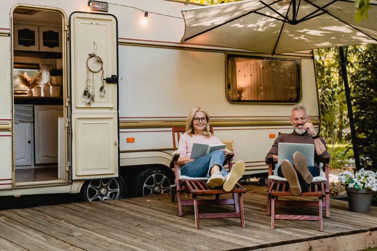 Senior joyful couple relaxing in the porch of thier motorhome with book and laptop