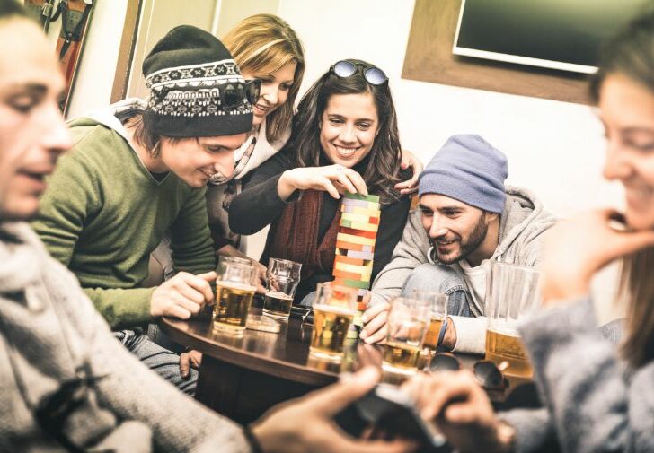 Happy friends playing table board game while drinking beer