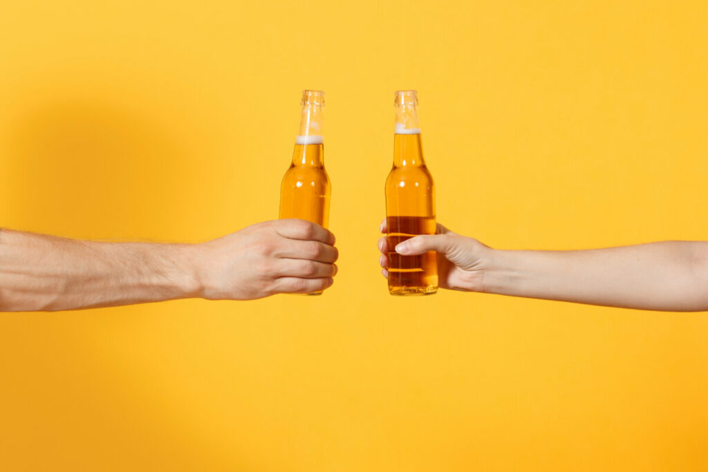 Close-up of two hands holding beer bottles, the kind of open container barred on Greyhound, FlixBus, and Megabus