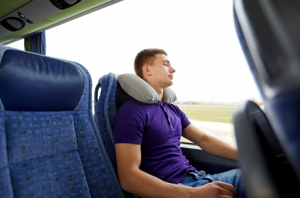 Male passenger sleeping with neck pillow inside a bus