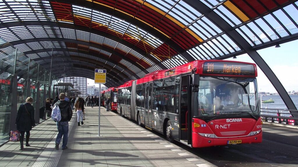 Modern bus terminal bustling with commuters, vibrant architecture, and scenic waterfront views.