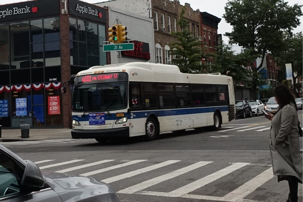 Busy urban street scene with Steinway St Q101 bus, pedestrians, and local bank in view.