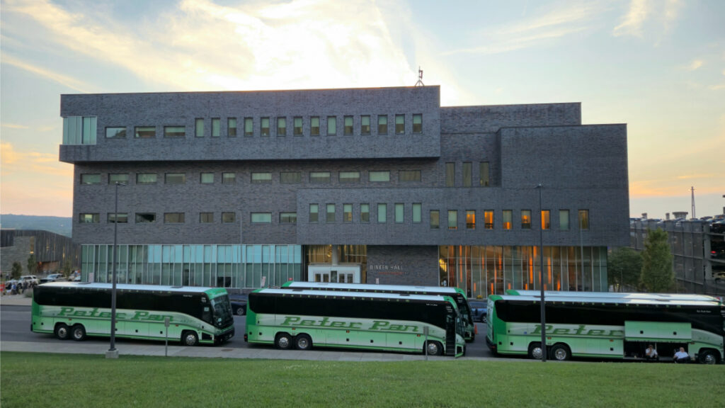 Dineen Hall with green Peter Pan buses parked in front during sunset.