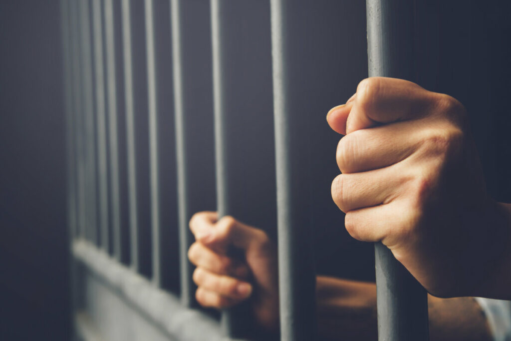 Close-up of hands gripping the jail bars from behind