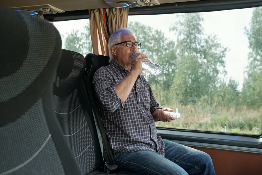 Old man on the bus taking a medicine and drinking water from a water bottle