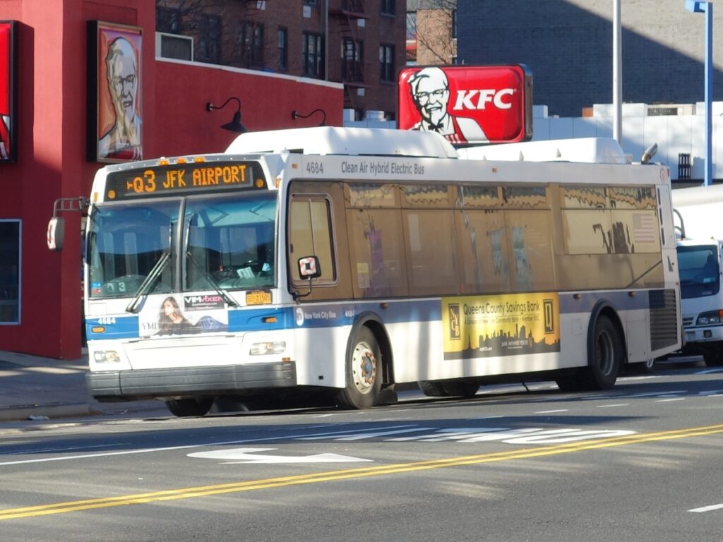 New York City Q3 bus to JFK Airport near KFC, showcasing urban public transit and advertising.