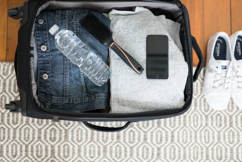 A small black carry-on suitcase packed with travel gear and a water bottle.