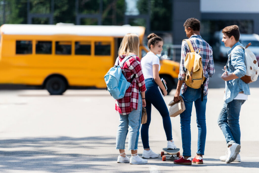 Teens with a skateboard close to a yellow school bus